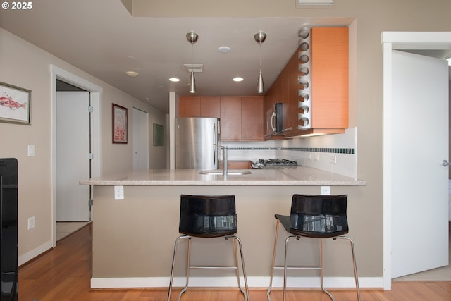 kitchen with a sink, light wood-style floors, appliances with stainless steel finishes, a peninsula, and decorative backsplash