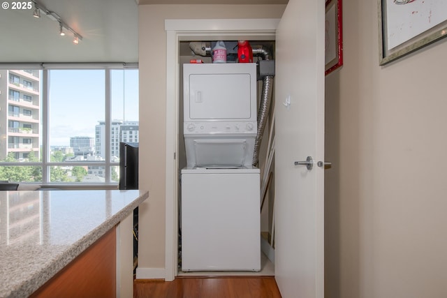 laundry room featuring a city view, wood finished floors, rail lighting, stacked washer / drying machine, and laundry area