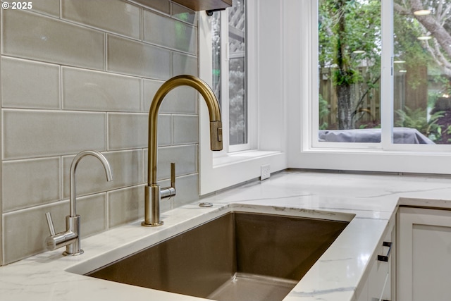 kitchen view of a sink, light stone countertops, tasteful backsplash, and white cabinetry