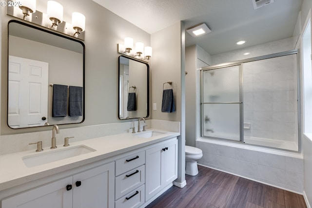 bathroom with wood finished floors, toilet, tiled shower / bath, and double vanity