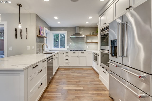 kitchen featuring stainless steel appliances, open shelves, a sink, wall chimney range hood, and recessed lighting