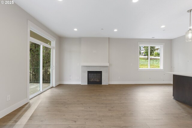 unfurnished living room with a tiled fireplace and light wood-type flooring