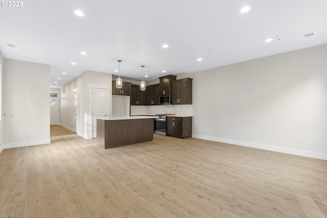 kitchen with stainless steel range with gas stovetop, light hardwood / wood-style floors, a kitchen island, decorative light fixtures, and white fridge