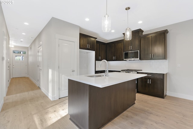 kitchen with sink, a kitchen island with sink, dark brown cabinets, light hardwood / wood-style floors, and decorative backsplash