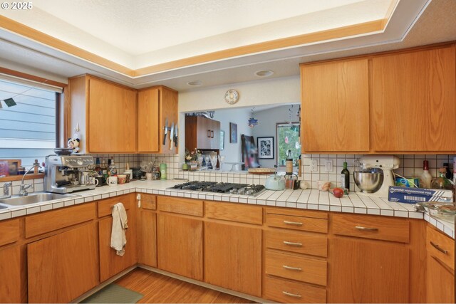 kitchen with stainless steel gas stovetop, backsplash, light countertops, light wood-style floors, and a sink