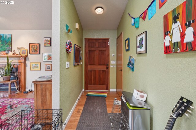 corridor with wood finished floors, a textured wall, and baseboards