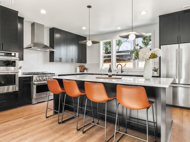 kitchen featuring a kitchen island, wall chimney exhaust hood, high quality appliances, and hanging light fixtures