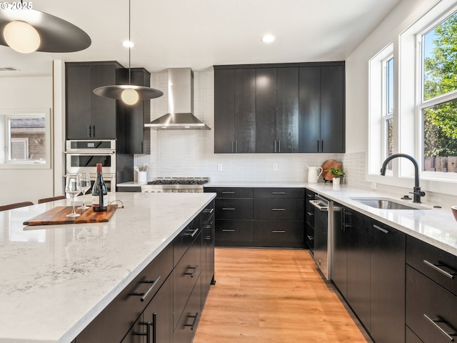 kitchen with sink, stainless steel double oven, hanging light fixtures, light hardwood / wood-style floors, and wall chimney range hood