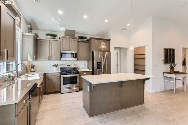 kitchen featuring appliances with stainless steel finishes, a sink, light wood-type flooring, a kitchen island, and vaulted ceiling