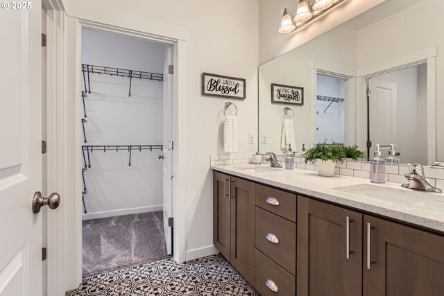 full bathroom with double vanity, a spacious closet, and baseboards