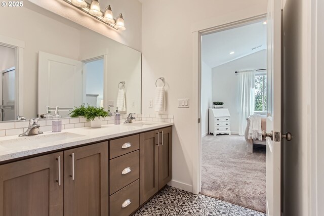 bathroom with vaulted ceiling, double vanity, baseboards, tasteful backsplash, and ensuite bathroom