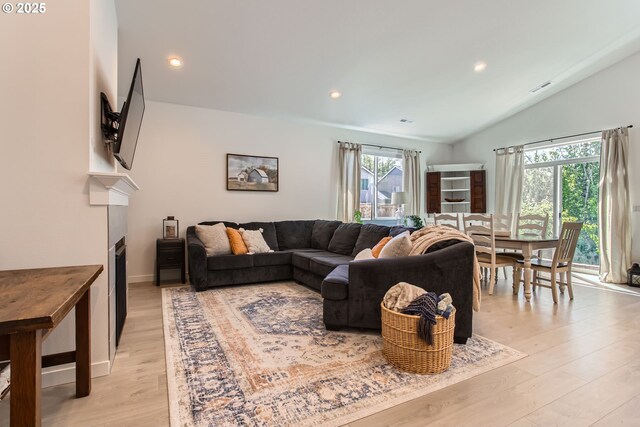 living area featuring light wood-style flooring, a fireplace, recessed lighting, and lofted ceiling