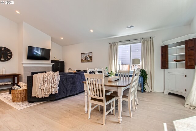 dining room featuring light wood finished floors, lofted ceiling, a fireplace, and recessed lighting