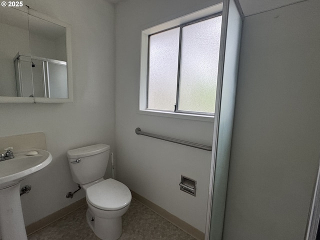 bathroom with a shower with shower door, baseboards, toilet, and a sink