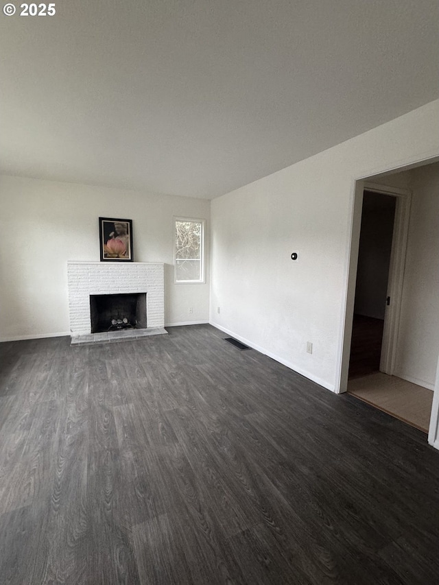 unfurnished living room featuring visible vents, baseboards, a brick fireplace, and dark wood-style flooring