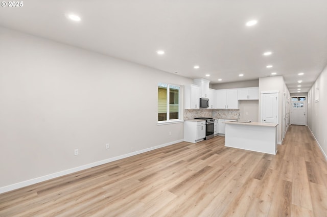 kitchen with white cabinetry, a center island, backsplash, light hardwood / wood-style floors, and appliances with stainless steel finishes