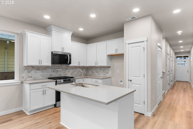 kitchen with sink, light hardwood / wood-style flooring, an island with sink, white cabinetry, and stainless steel appliances