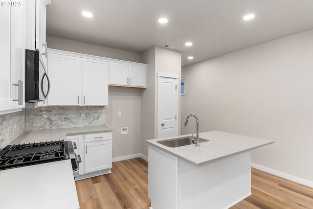 kitchen with sink, light hardwood / wood-style flooring, decorative backsplash, an island with sink, and white cabinetry