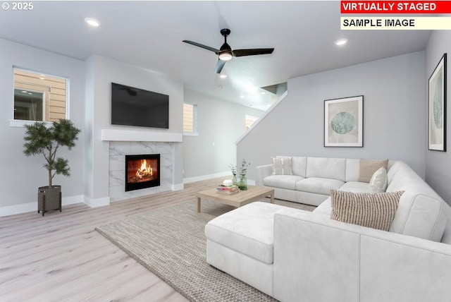 living room with ceiling fan, a fireplace, and light wood-type flooring