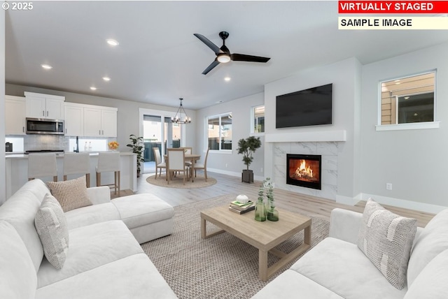 living room featuring a premium fireplace, ceiling fan with notable chandelier, and light wood-type flooring