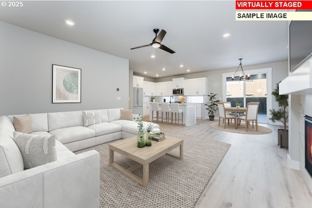 living room featuring ceiling fan with notable chandelier and light hardwood / wood-style flooring