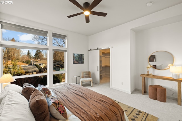 carpeted bedroom with a spacious closet, a barn door, and ceiling fan