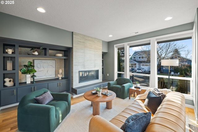 living room featuring a tile fireplace, a textured ceiling, and light wood-type flooring