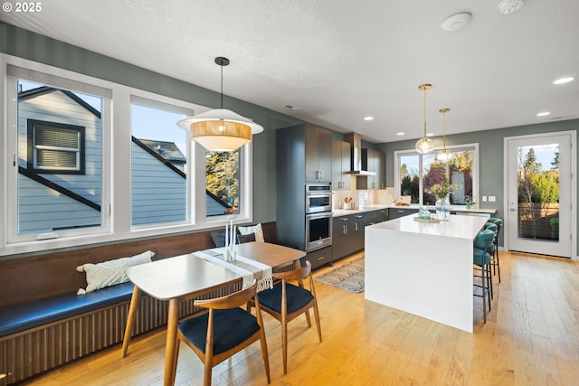 kitchen featuring hanging light fixtures, a kitchen bar, wall chimney range hood, and light hardwood / wood-style floors