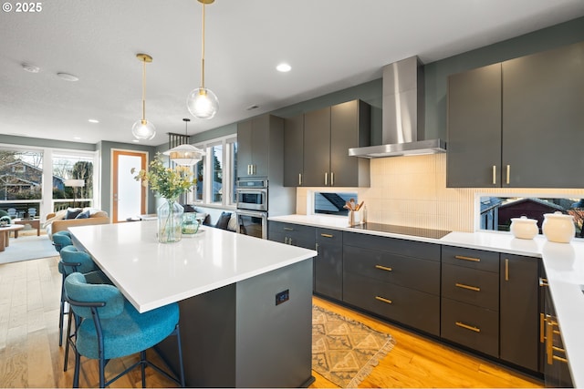 kitchen featuring a breakfast bar, decorative light fixtures, tasteful backsplash, wall chimney range hood, and black electric cooktop