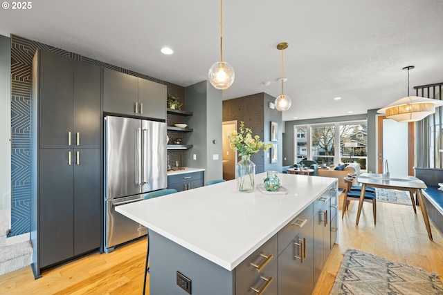 kitchen featuring pendant lighting, high quality fridge, a kitchen island, and light hardwood / wood-style flooring