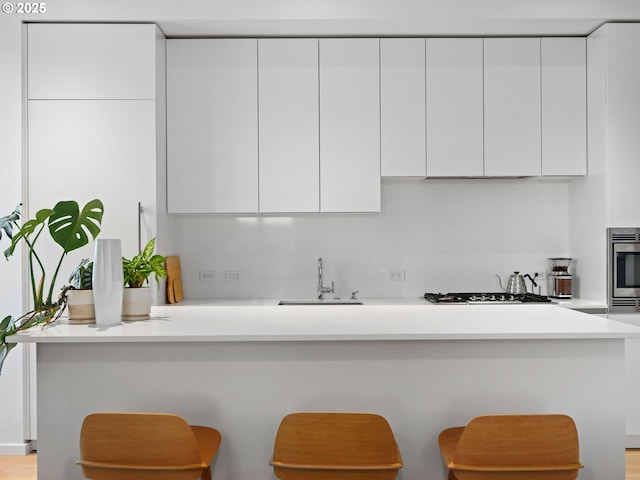 kitchen featuring sink, white cabinetry, stainless steel gas cooktop, a kitchen bar, and oven