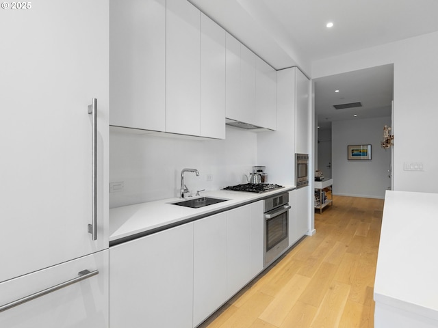 kitchen with light wood-type flooring, appliances with stainless steel finishes, sink, and white cabinets