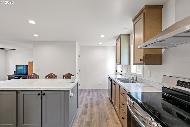 kitchen with gray cabinets, a sink, light countertops, appliances with stainless steel finishes, and wall chimney exhaust hood