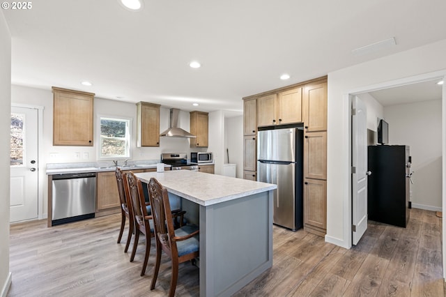 kitchen with appliances with stainless steel finishes, light wood-style flooring, light countertops, and wall chimney range hood