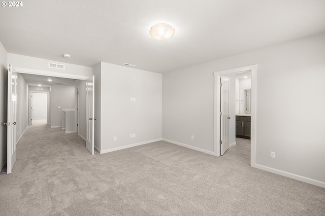 unfurnished bedroom featuring light carpet and ensuite bath