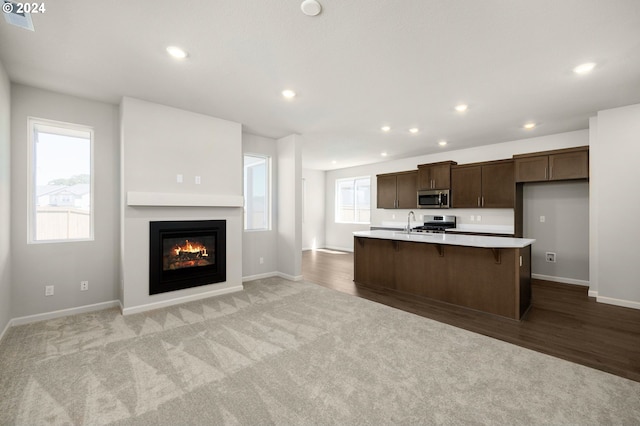 kitchen with a kitchen bar, light carpet, a center island with sink, and stainless steel appliances