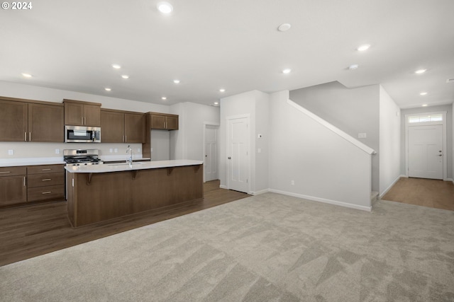 kitchen with sink, an island with sink, a breakfast bar, carpet, and appliances with stainless steel finishes