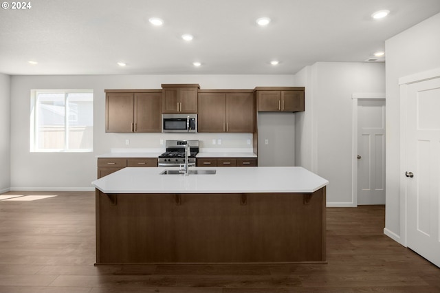 kitchen with dark hardwood / wood-style flooring, stainless steel appliances, a kitchen island with sink, and sink