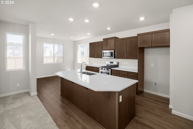 kitchen with sink, stainless steel appliances, a kitchen breakfast bar, dark hardwood / wood-style flooring, and a kitchen island with sink