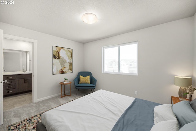 bedroom with ensuite bathroom, sink, light colored carpet, and a textured ceiling