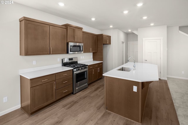 kitchen with a center island with sink, sink, light wood-type flooring, and stainless steel appliances