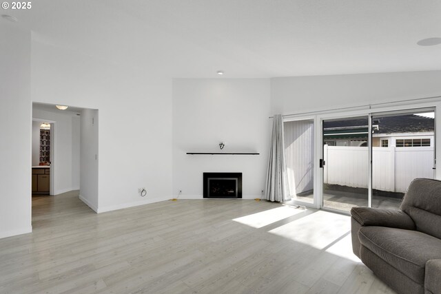 living area featuring high vaulted ceiling, baseboards, light wood-style floors, and a fireplace