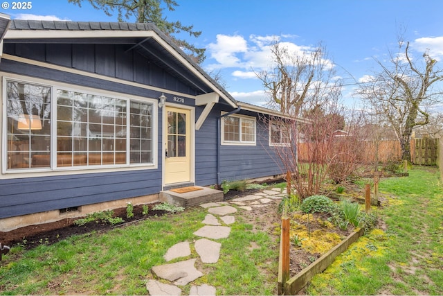 exterior space featuring board and batten siding, fence, entry steps, a yard, and a vegetable garden