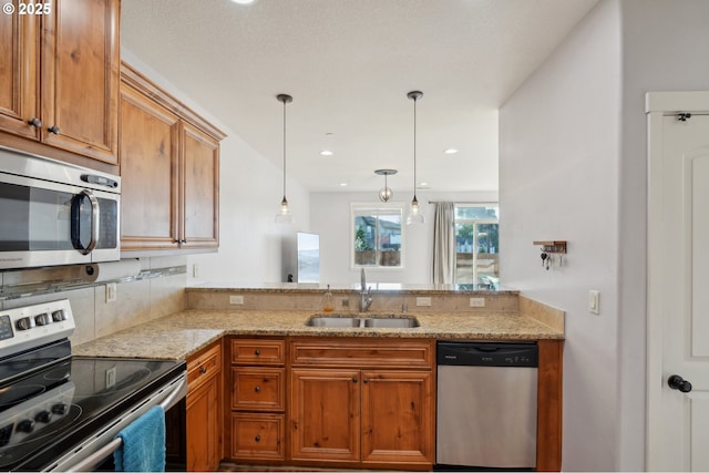 229 N 33rd Ct, Ridgefield, WA 98642 - kitchen with stainless steel appliances, a sink, light stone countertops, decorative light fixtures, and brown cabinets