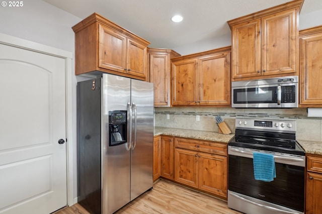 229 N 33rd Ct, Ridgefield, WA 98642 - kitchen with appliances with stainless steel finishes, backsplash, light stone countertops, light wood-style floors, and brown cabinets