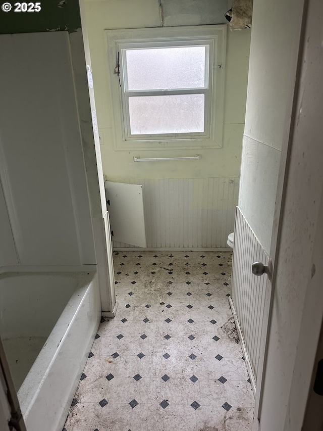 bathroom with tile patterned floors, wainscoting, a bathing tub, and toilet