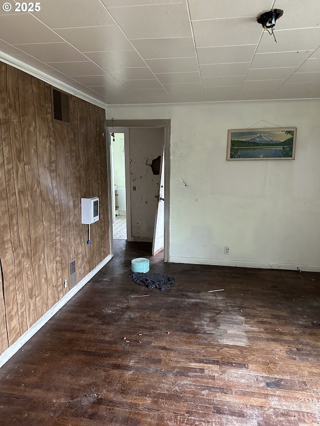 spare room with wooden walls, visible vents, baseboards, and hardwood / wood-style flooring