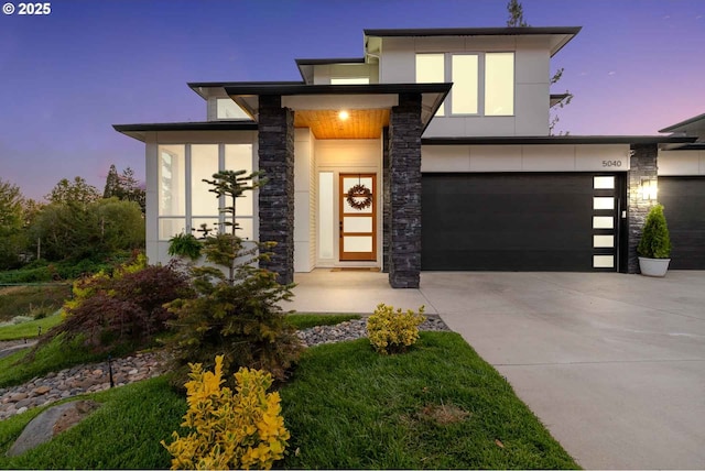 contemporary house with stone siding, stucco siding, concrete driveway, and a garage