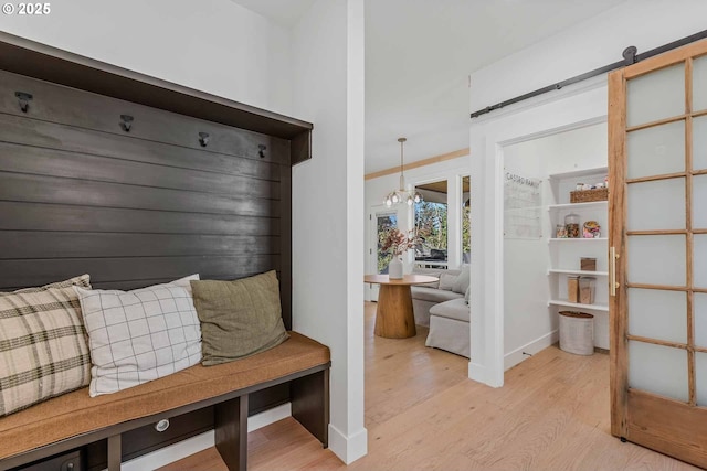 mudroom with light wood-type flooring, a barn door, baseboards, and a chandelier