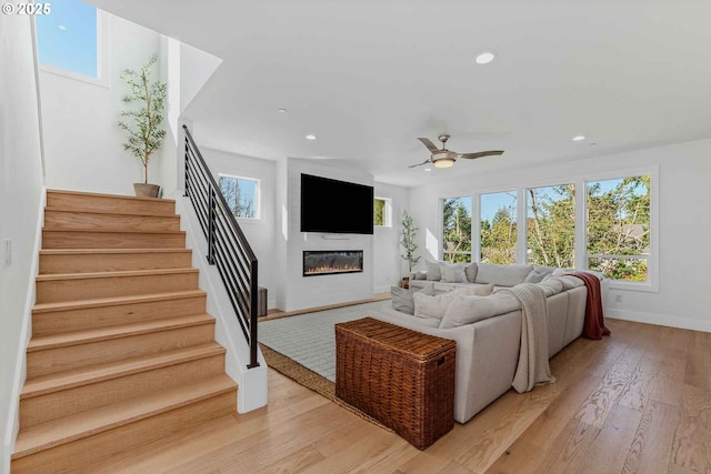 living room with stairs, light wood-type flooring, recessed lighting, a glass covered fireplace, and a ceiling fan